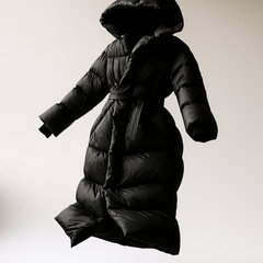 Black long belted puffer jacket for women by Christine Brewer, featuring a stylish floating design and cozy insulation.