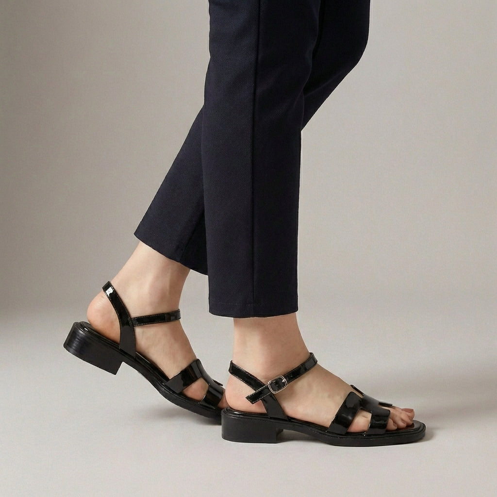 Black ankle-length flat sandals with ankle strap and buckle by Christine Brewer, featuring a sleek and comfortable design.