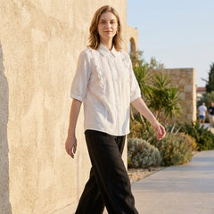 Woman wearing a denim ruffle summer blouse by Christine Brewer, casual top with ruffled details, outdoors lifestyle shot.