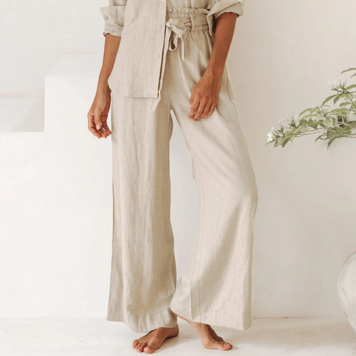 Light beige linen wide-leg trousers for women with a loose pull-on design, styled casually on a model.