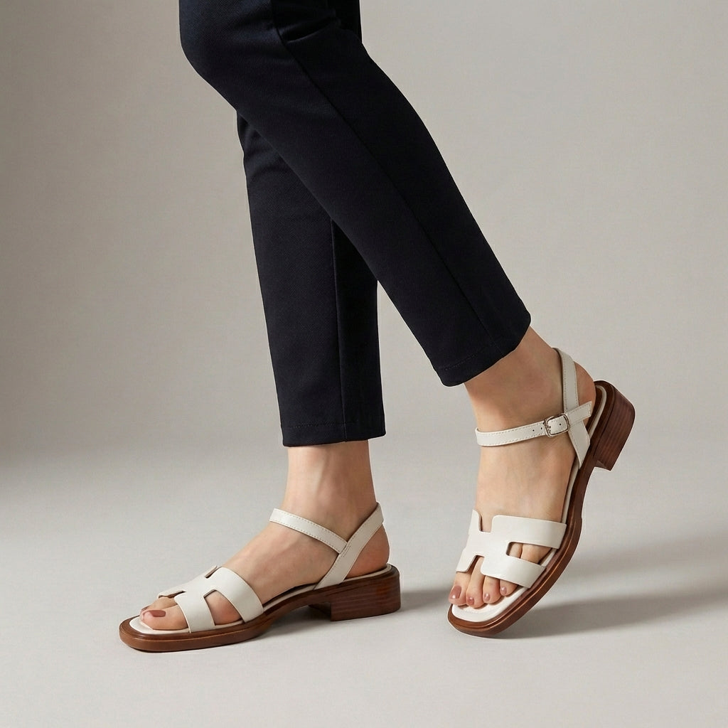 White ankle-length flat sandals with ankle strap and buckle by Christine Brewer, featuring a simple, stylish design.