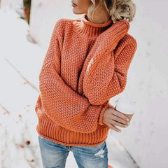 Orange knit turtleneck sweater for women by Christine Brewer, featuring a loose, boho-inspired design with a beach hut backdrop.