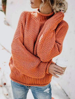Orange knit turtleneck sweater for women by Christine Brewer, featuring a loose, boho-inspired design with a beach hut backdrop.