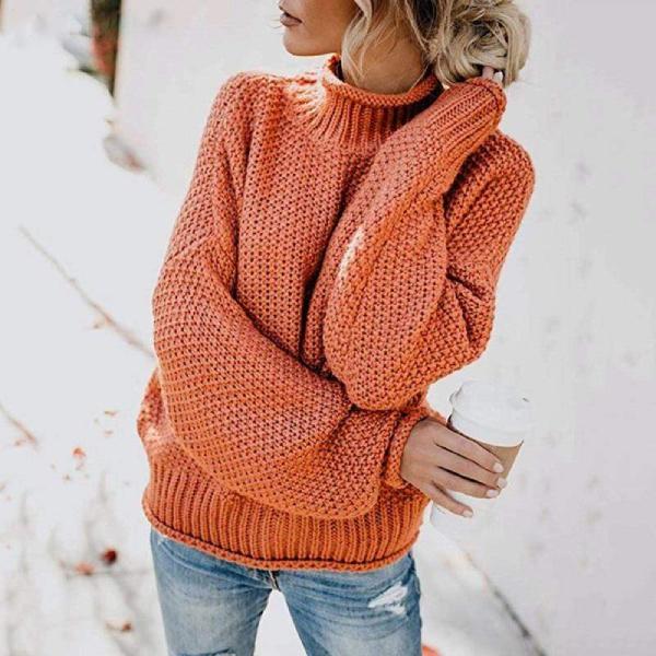 Orange knit turtleneck sweater for women by Christine Brewer, featuring a loose, boho-inspired design with a beach hut backdrop.