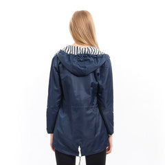 Victoria women's waterproof rain coat with hood and drawstring, designed by Christine Brewer, shown on a model outdoors.