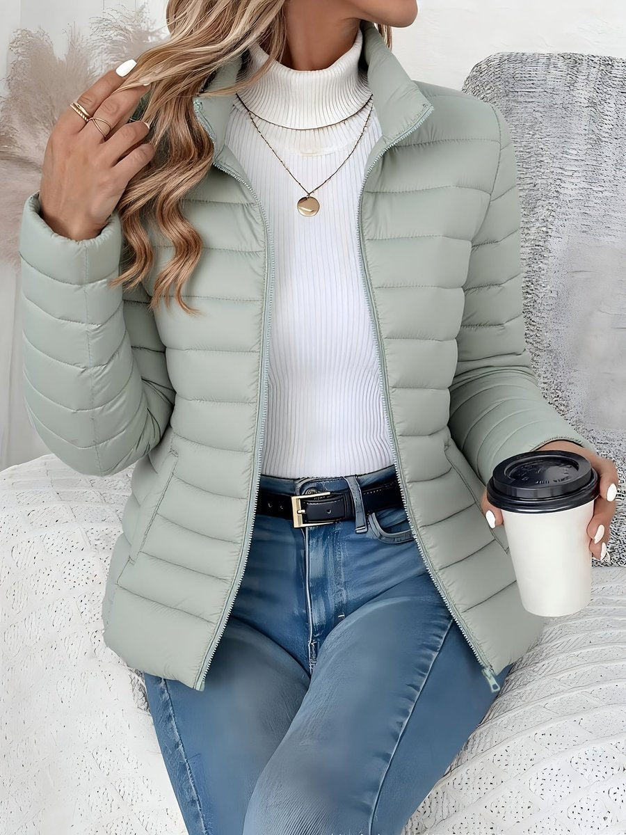 Women's lightweight quilted puffer coat with stand collar and zip-up front by Christine Brewer, shown in a stylish outdoor setting.