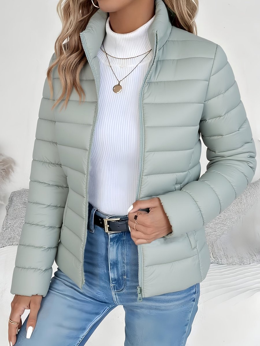 Women's lightweight quilted puffer coat with stand collar and zip-up front by Christine Brewer, shown in a stylish outdoor setting.