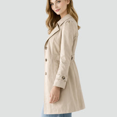 Christine Brewer women's tailored mid-length double-breasted trench coat hanging on a rack. Classic beige color with belt and button details.