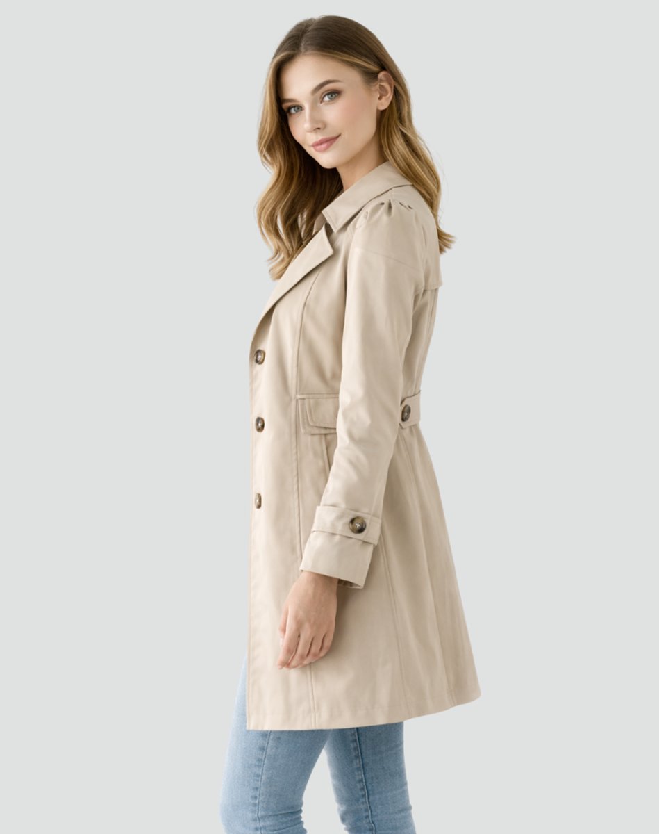 Christine Brewer women's tailored mid-length double-breasted trench coat hanging on a rack. Classic beige color with belt and button details.